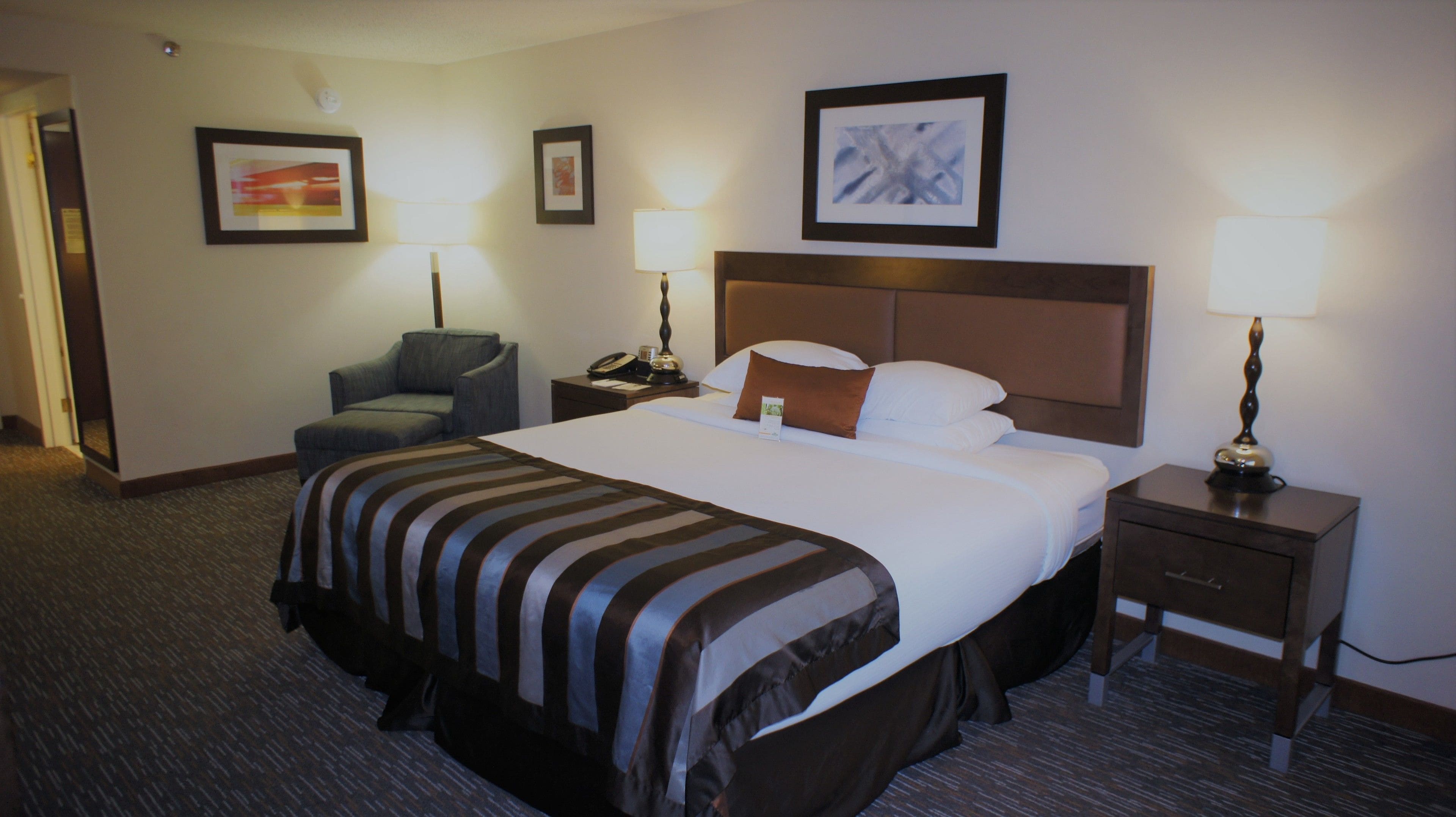 A hotel room with a large bed, two bedside tables, a chair, and framed artwork on the walls.