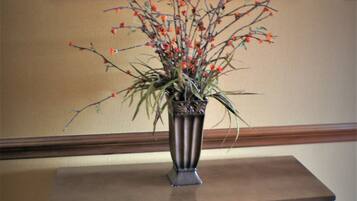 Una pequeña mesa de madera con un florero metálico lleno de flores rojas.