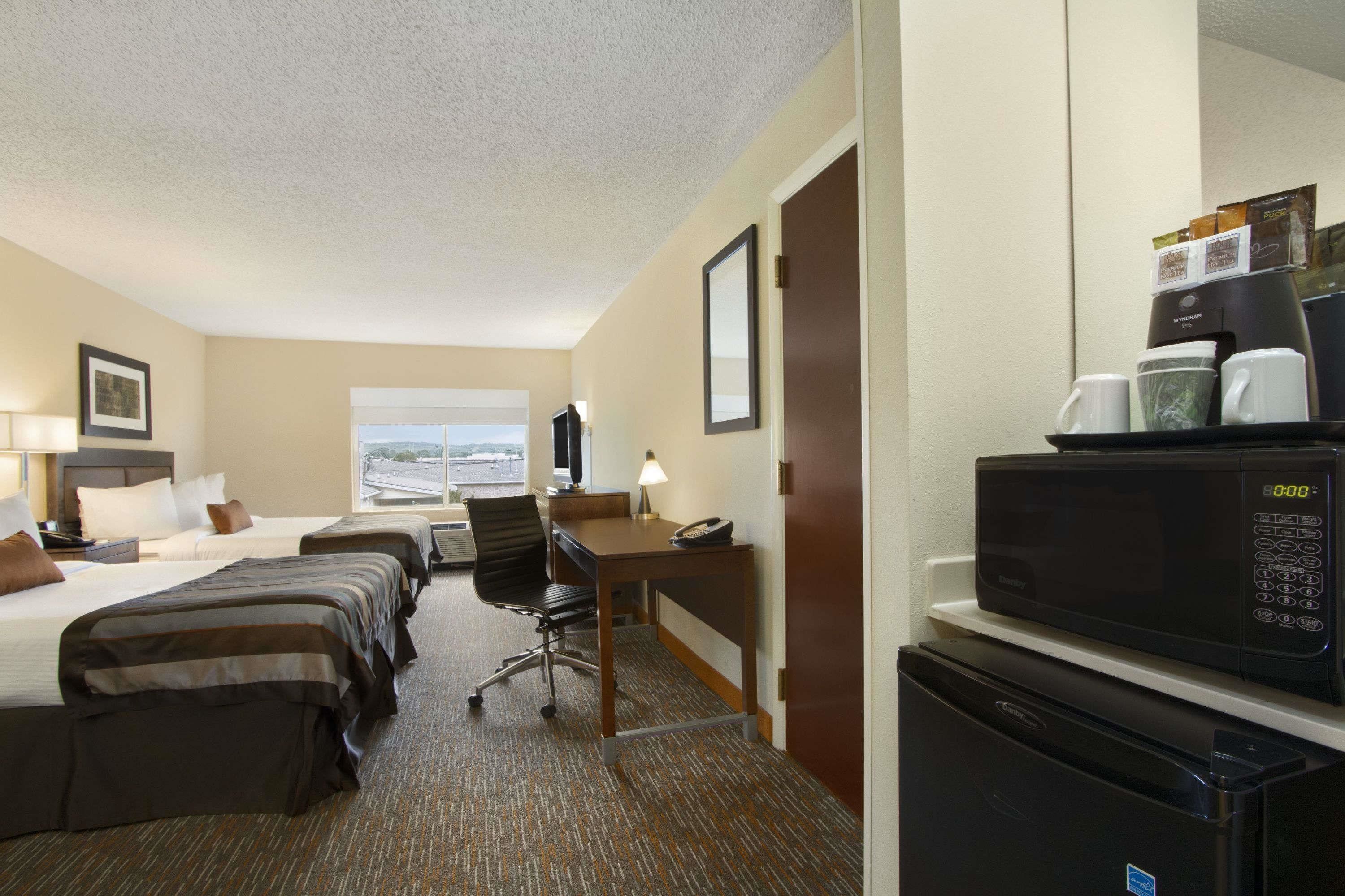 Une chambre d’hôtel avec deux lits, un bureau, une chaise, un four à micro-ondes, un réfrigérateur et une machine à café.