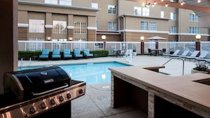 Zona de piscina exterior con una parrilla y sillones de descanso.
