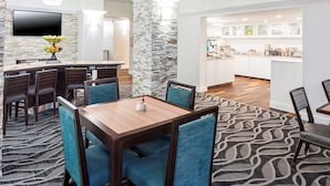 Un hall de hotel con comedor, cocina y televisor montado en la pared.