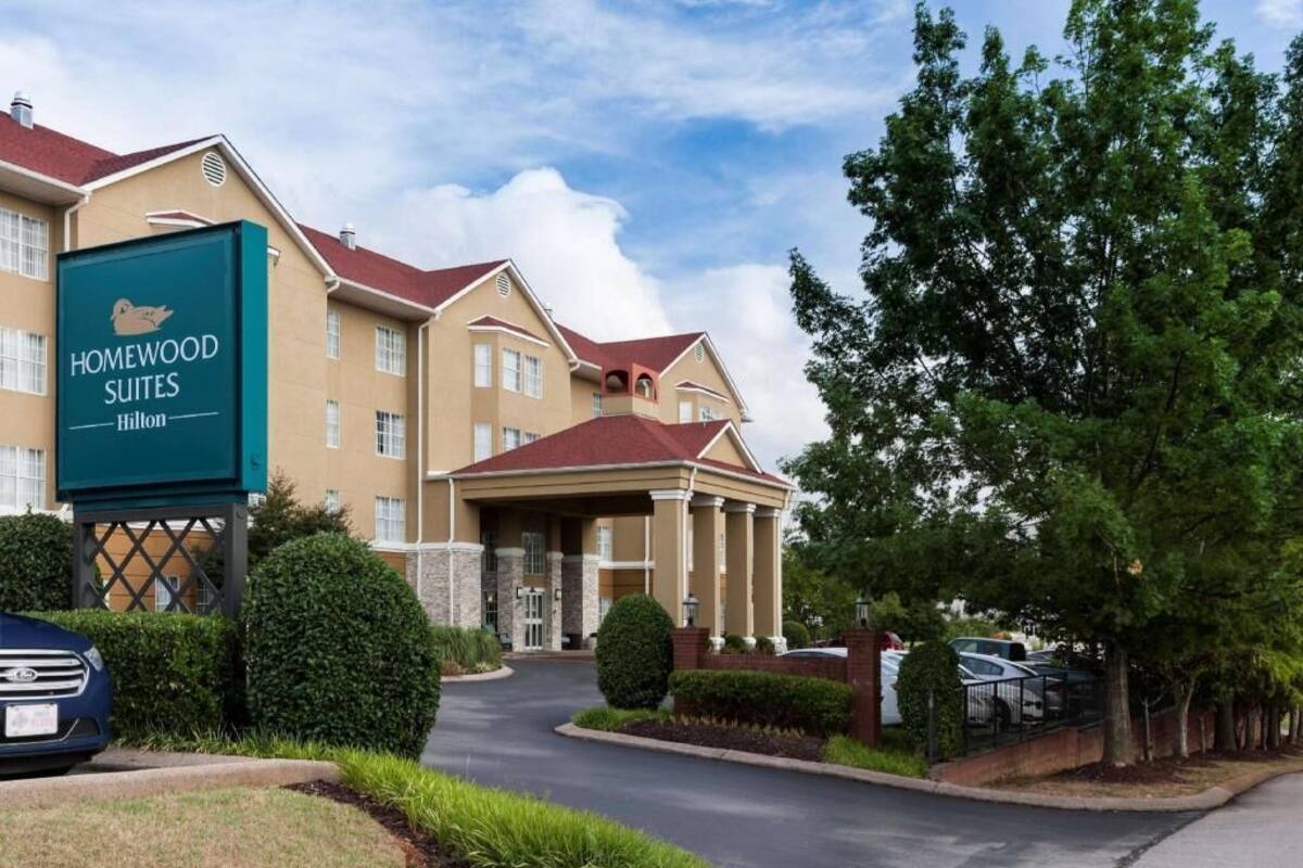 Een hotel met een bord waarop 'Homewood Suites Hilton' staat, een overdekte ingang en een parkeerplaats.