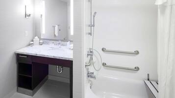 A modern bathroom with a white vanity, a large mirror, a bathtub with grab bars, and a shower with a handheld showerhead.