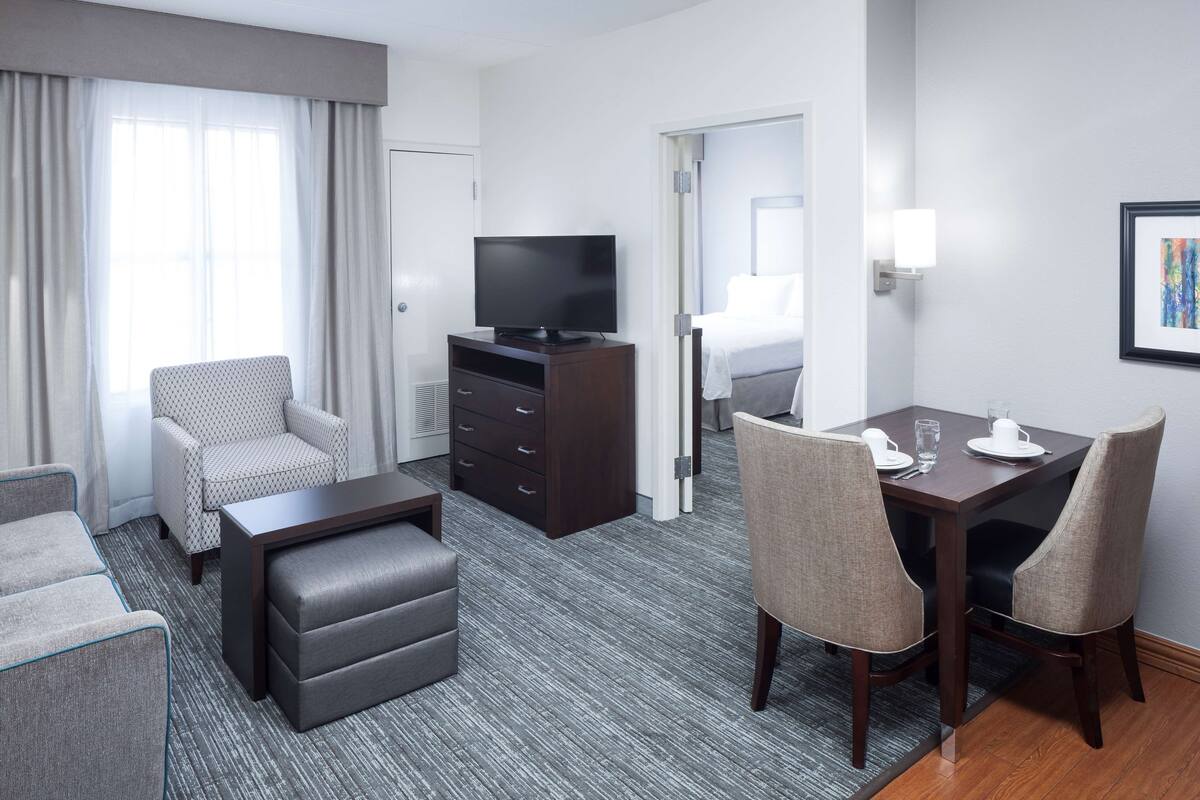 Een hotelkamer met een zithoek, een televisie, een eettafel met stoelen en een bed.