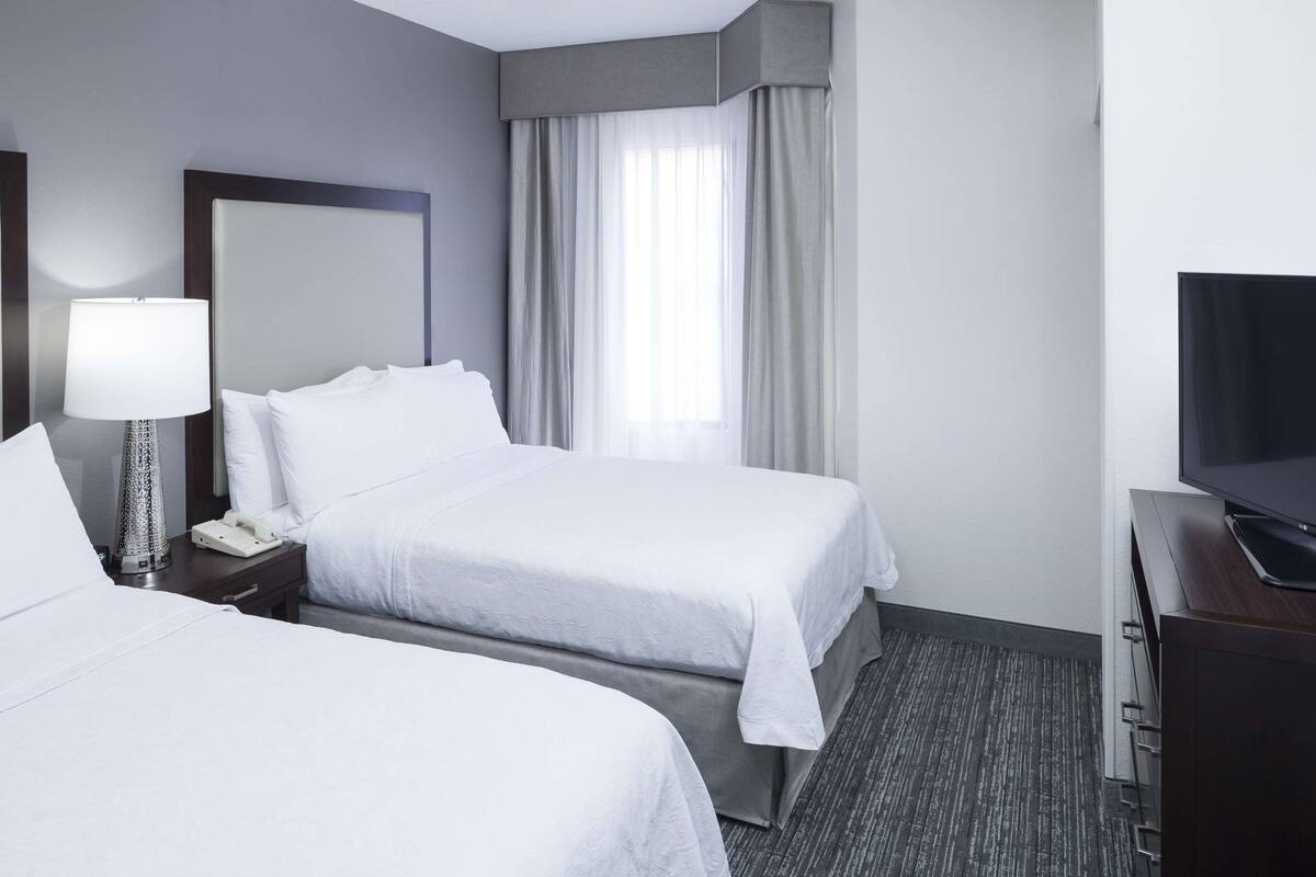 Een hotelkamer met twee bedden, een bureau met een televisie, een lamp en een raam met gordijnen.