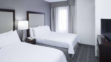 A hotel room with two beds, a desk with a TV, a lamp, and a window with curtains.