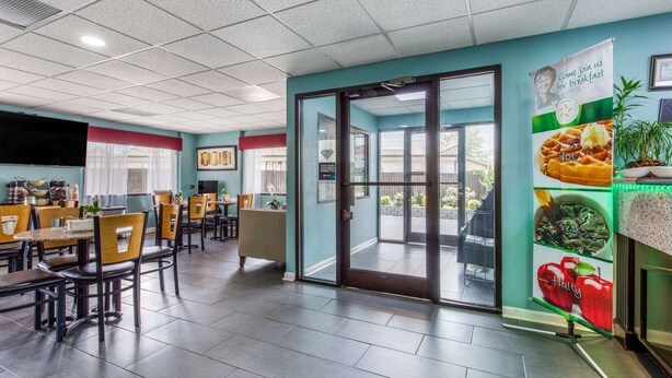 A restaurant with a modern interior, featuring a large dining area with tables and chairs, a kitchen area with a TV, and a glass door leading outside. - Quality Inn Kingston Springs (Kingston Springs)