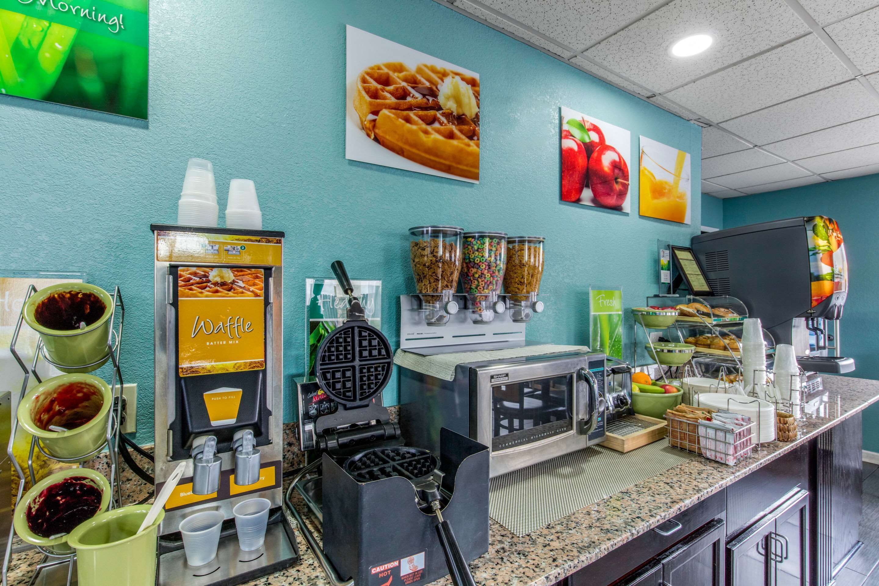 A breakfast bar with waffle and waffle iron machines, beverage dispensers, and a coffee maker.