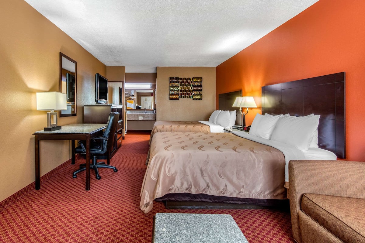 A hotel room with a bed, a desk, a chair, a TV, and a small table.