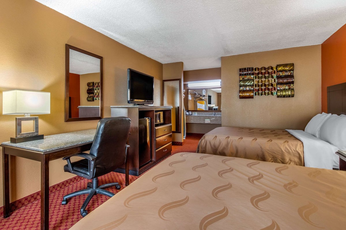 A hotel room with a bed, desk, chair, television, and a wall with patterned artwork.