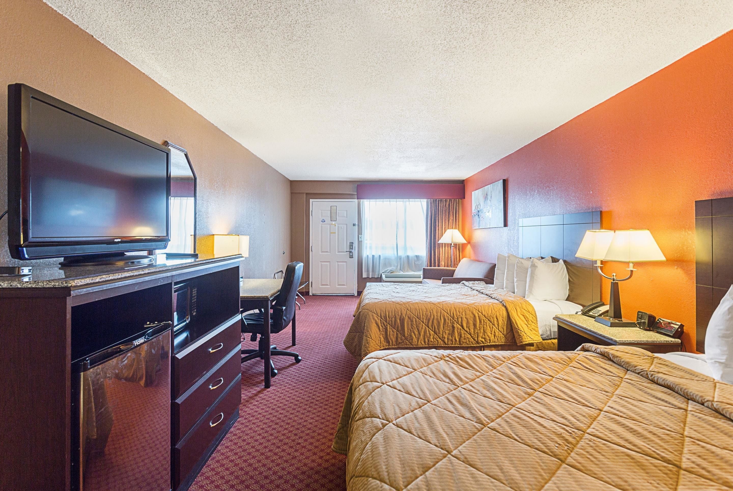 A hotel room with two beds, a desk with a chair, a television, and a microwave.