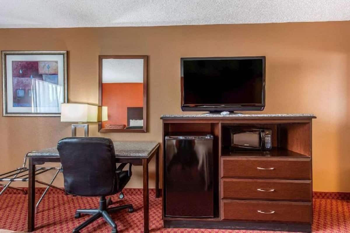 A hotel room with a desk, chair, television, refrigerator, and microwave.