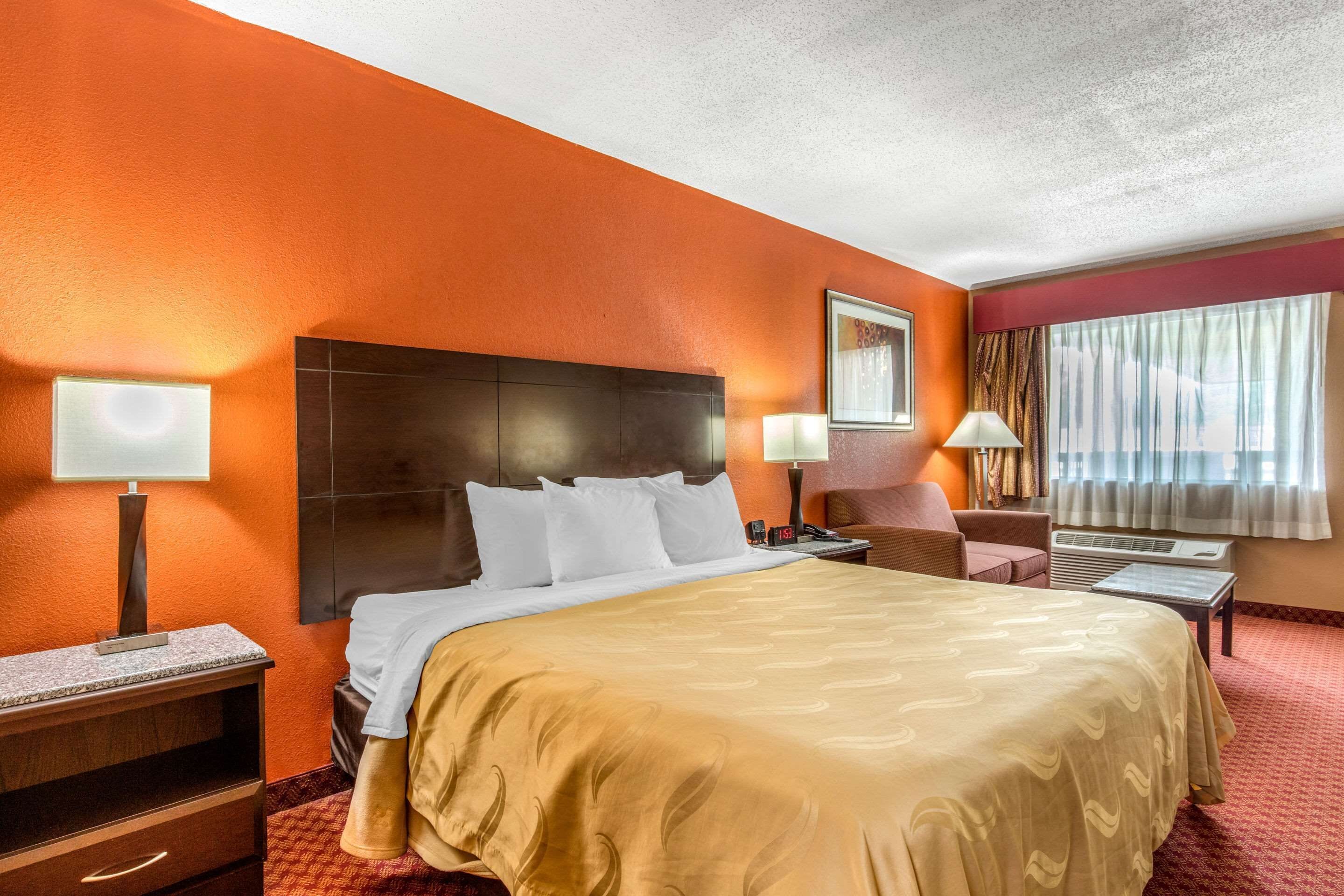 Een hotelkamer met een groot bed, een bureau, een stoel, een nachtkastje en een raam met gordijnen.