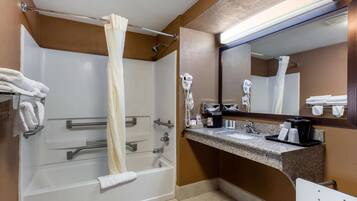 A hotel bathroom with a bathtub, a shower, a vanity with a mirror, and a towel rack.