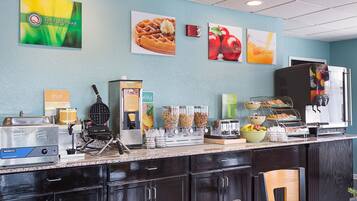 A breakfast bar with a waffle maker, coffee machine, and various food containers.