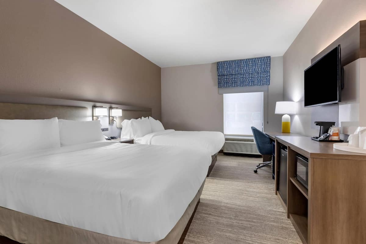 A hotel room with a large bed, a desk with a computer, a TV, and a window with a view of the outside.