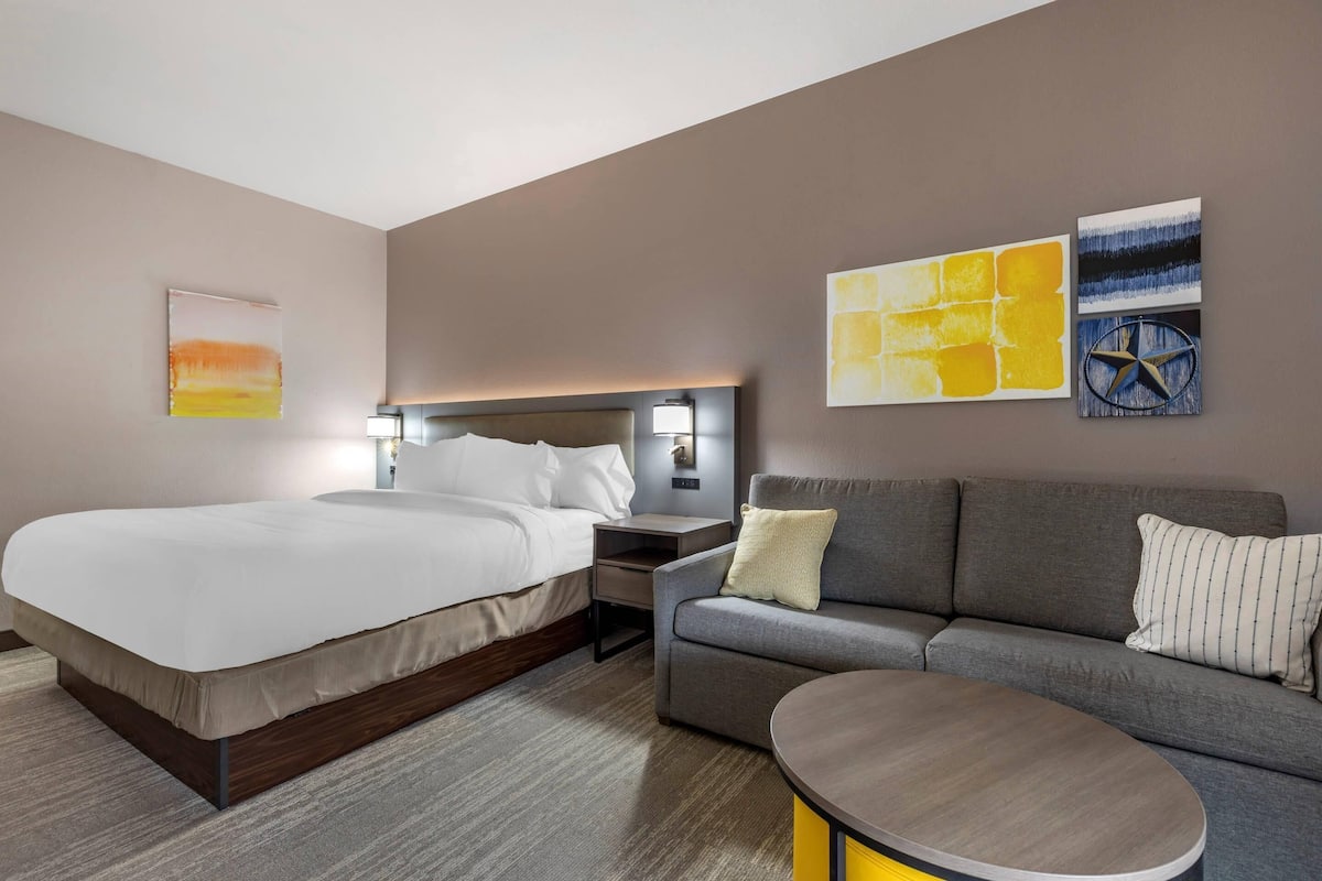 A modern hotel room with a large bed, a sofa, a small table, and artwork on the walls.