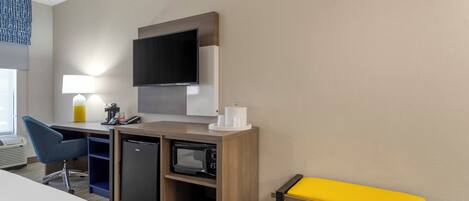 Habitación de hotel con escritorio, silla, microondas y un pequeño banco.