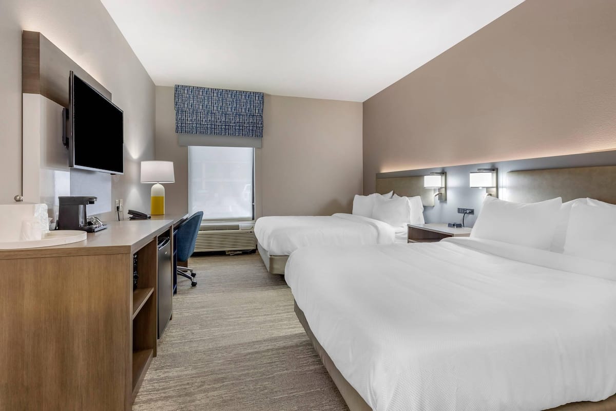 A hotel room with a large bed, a desk with a computer, a TV, and a window with a view.