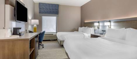 A hotel room with a large bed, a desk with a computer, a TV, and a window with a view.