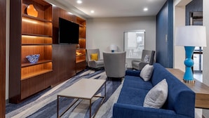 A modern living room with a blue sofa, a wooden entertainment unit, and a flat-screen TV. - Comfort Inn - Weatherford (Weatherford)