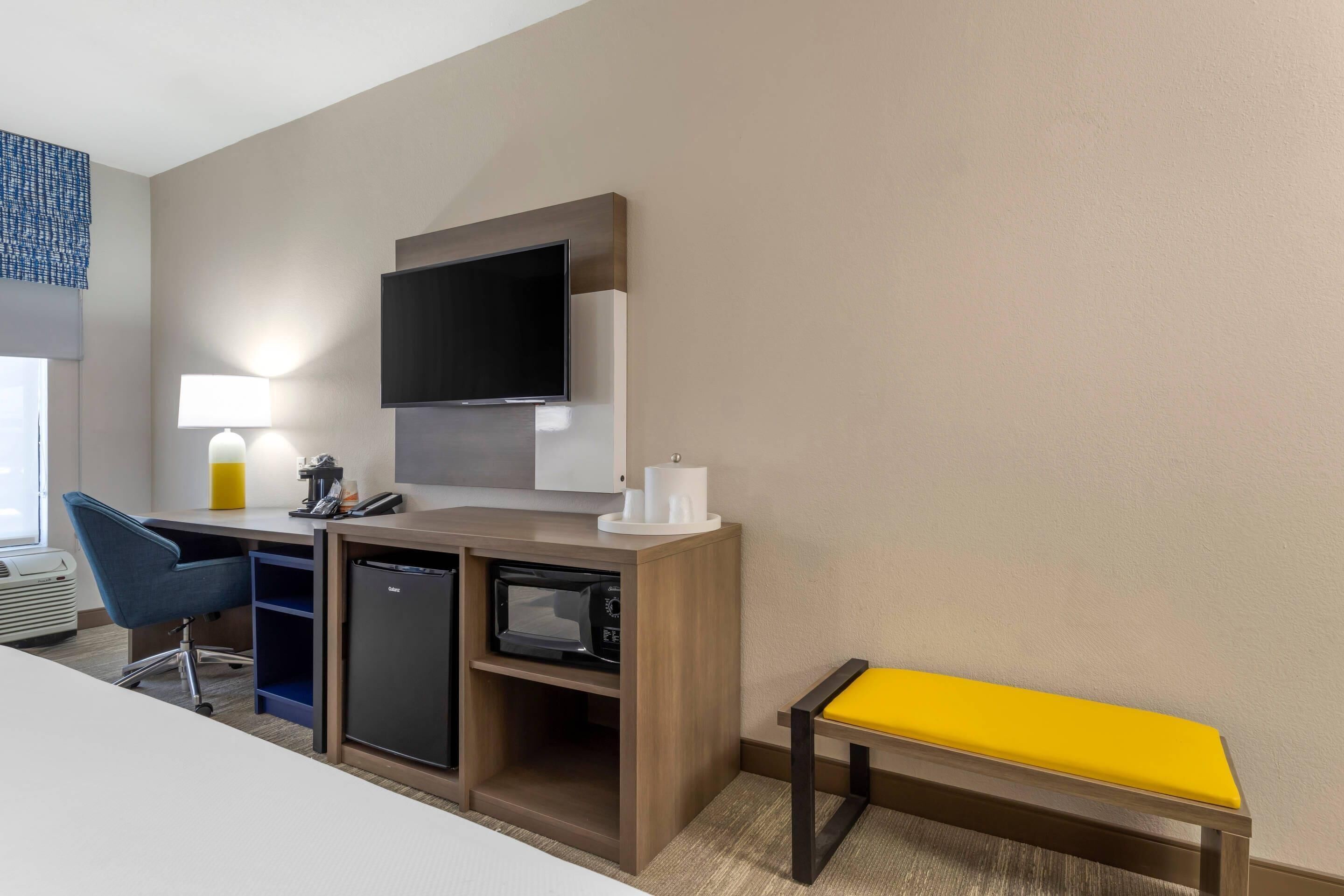Une chambre d’hôtel équipée d’un bureau, d’une chaise, d’une télévision et d’un petit banc.