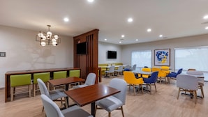 A modern dining area with wooden tables and chairs, a central seating area with a high backrest, and a flat-screen TV mounted on the wall. - Comfort Inn - Weatherford (Weatherford)