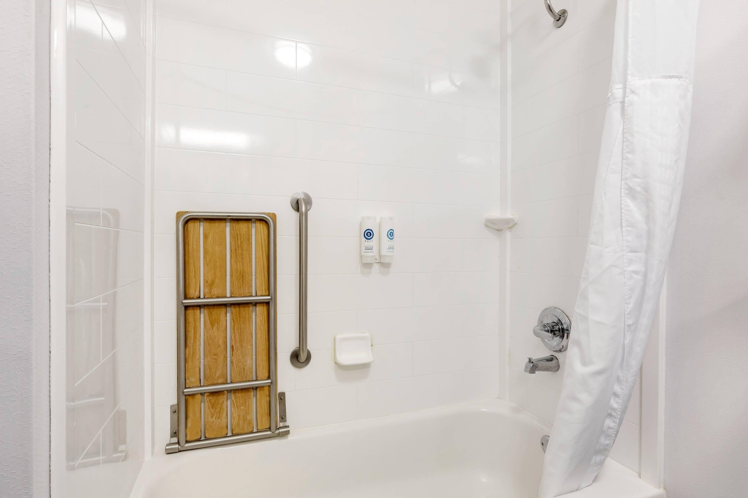 A white-tiled shower with a wooden window, a grab bar, and two soap dispensers.