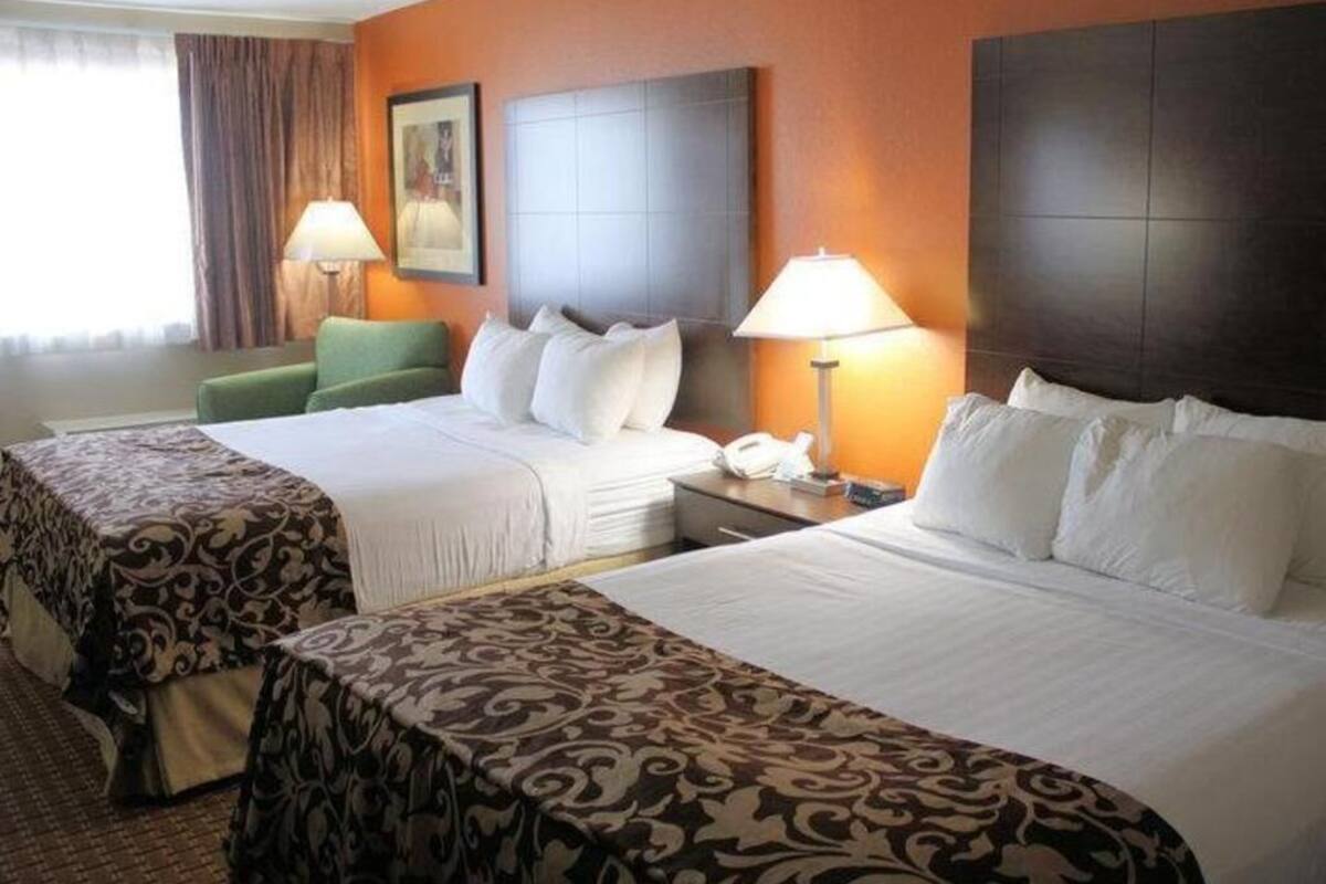 Ein Hotelzimmer mit zwei Betten, einem grünen Sessel, einem Nachttisch mit Lampe und einem Bild an der Wand.