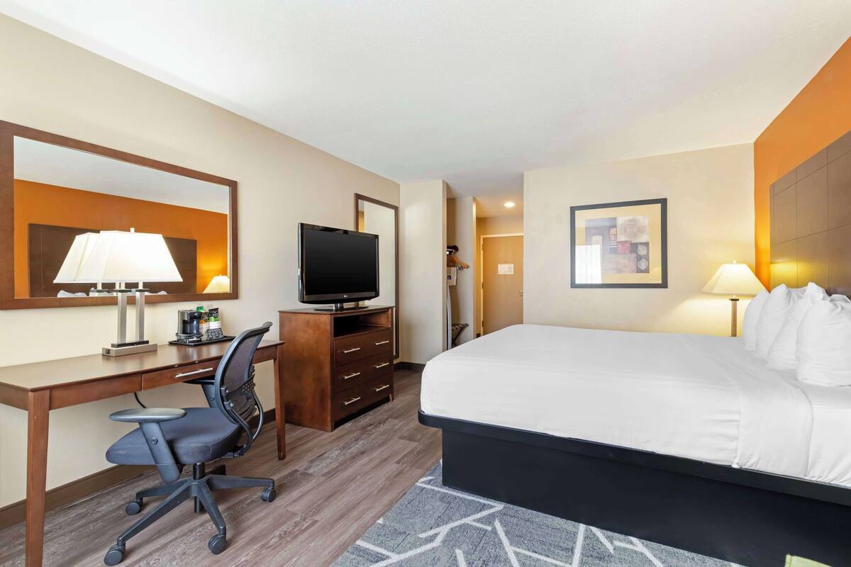 Ein Hotelzimmer mit Bett, Schreibtisch, Stuhl, Fernseher und Spiegel.