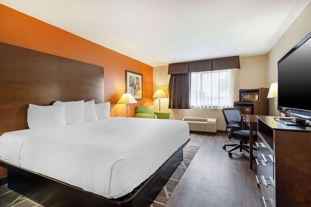 Ein Hotelzimmer mit einem großen Bett, einem Schreibtisch mit Computer, einem Sessel und einem Fernseher.