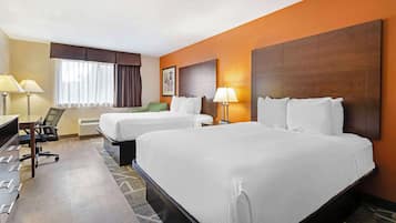 Habitación de hotel con dos camas, un escritorio con silla, una lámpara y un ventanal con cortinas.