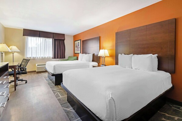 Une chambre d’hôtel avec deux lits, un bureau avec une chaise, une lampe et une fenêtre avec des rideaux.
