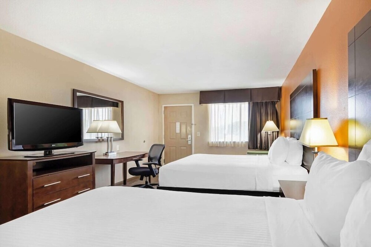 A hotel room with two beds, a TV, a desk with a chair, and lamps.
