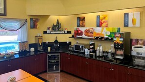 A hotel kitchen with a self-service breakfast area, including a coffee machine, microwave, and various food items. - Quality Inn & Suites Houston Northwest - Cypress (Houston)