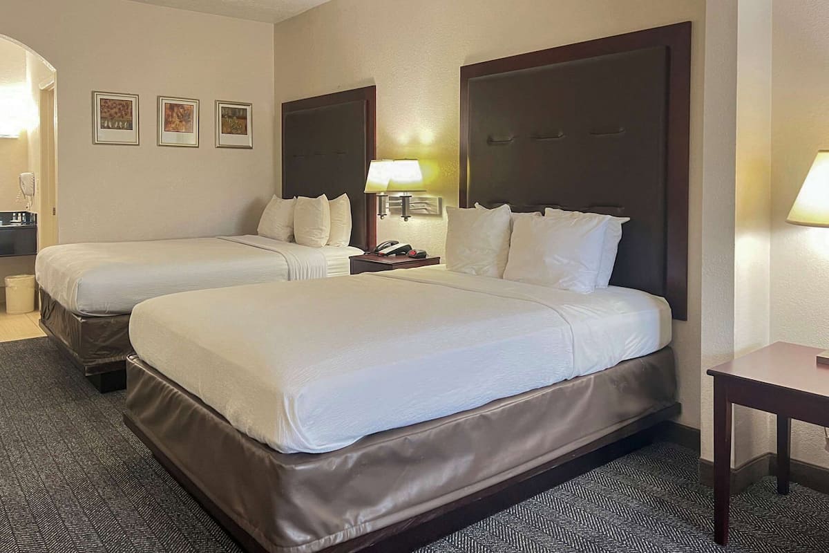A hotel room with two beds, a desk, a chair, a lamp, and a small table.