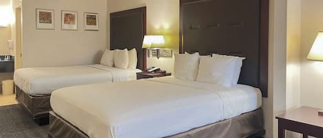 A hotel room with two beds, a nightstand with a lamp, and framed pictures on the wall.