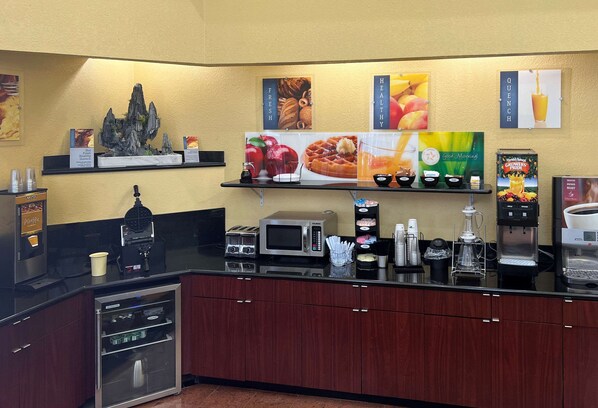 A breakfast bar with coffee machines, a microwave, and a coffee dispenser. There are signs for fresh and healthy options, and a sign for Quench juice.