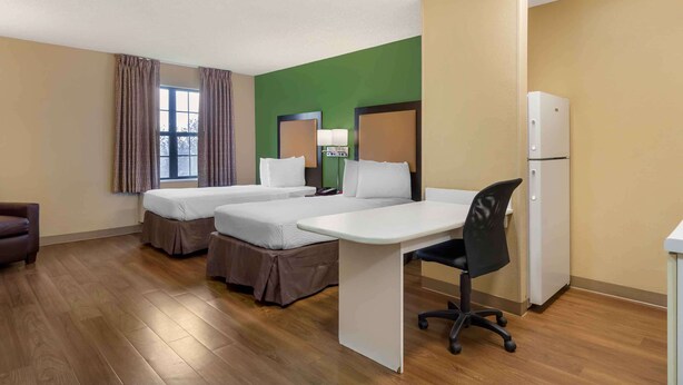 Une chambre d’hôtel avec deux lits, un bureau, une chaise, un réfrigérateur et une fenêtre avec des rideaux.