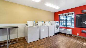 A laundry room with four washing machines, a table, and a window with blinds.