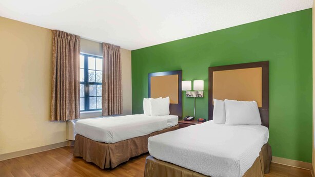 A hotel room with two beds, a window with curtains, a nightstand with a lamp, and a green wall. - Extended Stay America Suites Seattle Everett North (Everett)
