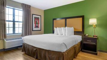A hotel room with a large bed, a bedside table with a lamp, a framed picture on the wall, and a window with curtains.