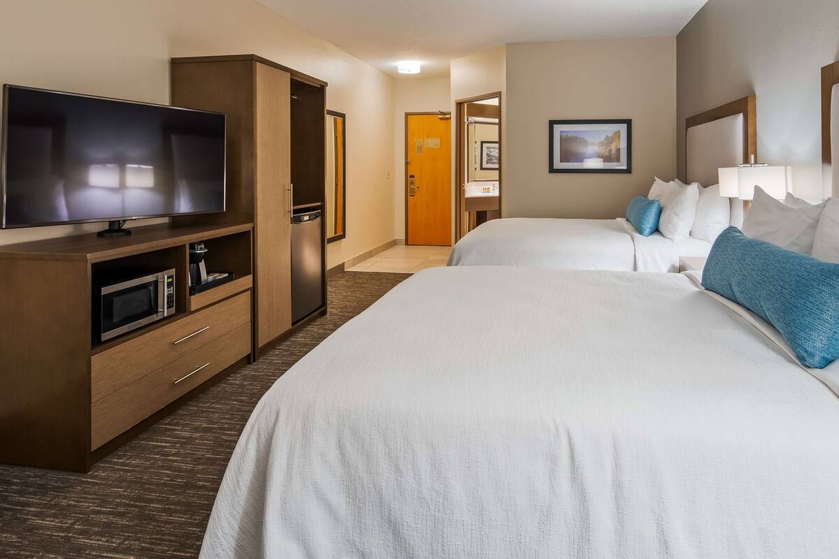A hotel room with two beds, a TV, a microwave, and a wardrobe.