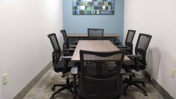 A conference room with a rectangular table, six black office chairs, and a blue abstract painting on the wall.