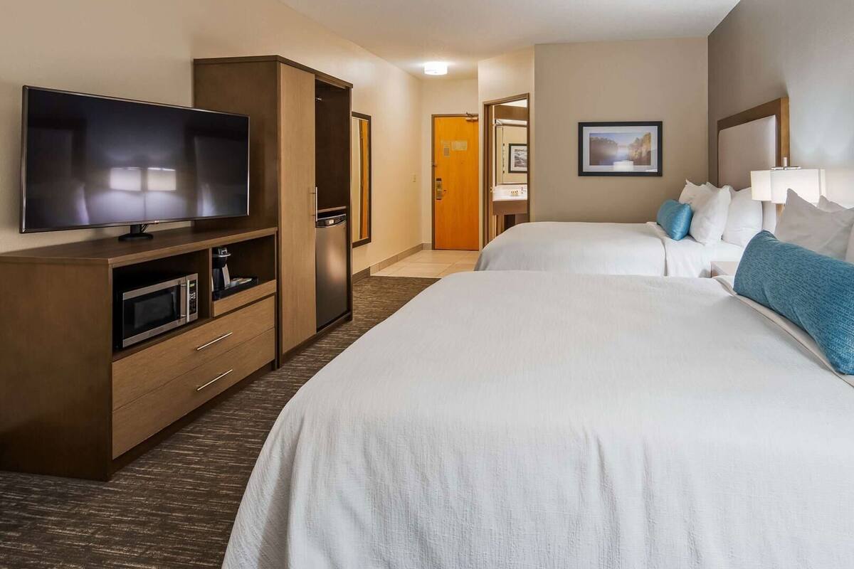 A hotel room with a TV, kitchenette, two beds, and a bathroom.