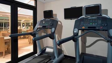 A fitness room with treadmills, a large window, and a view of the outdoor seating area.