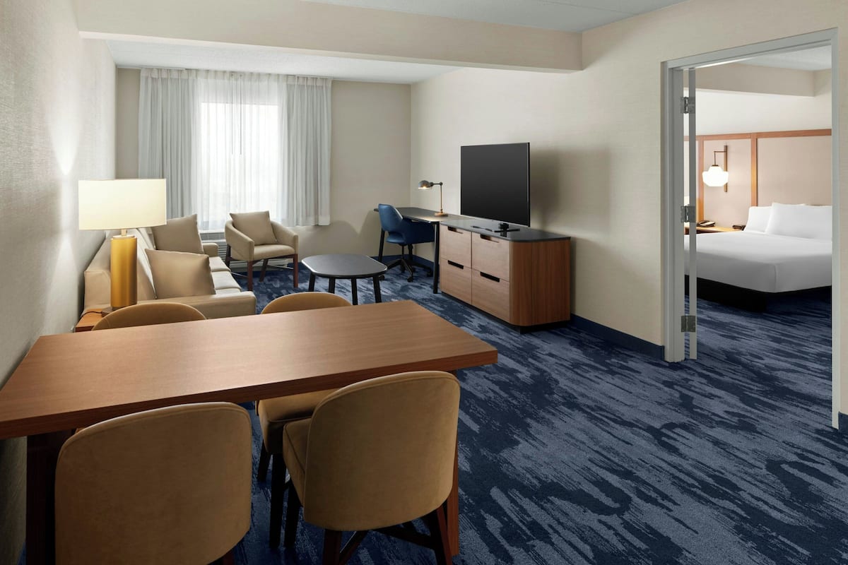 A hotel room with a wooden desk, two chairs, a television, a bed, and a small table with a lamp.
