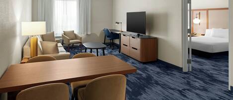A hotel room with a wooden desk, two chairs, a television, a bed, and a small table with a lamp.