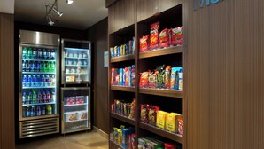 A corner market with refrigerated beverage dispensers and shelves stocked with snacks and packaged goods.