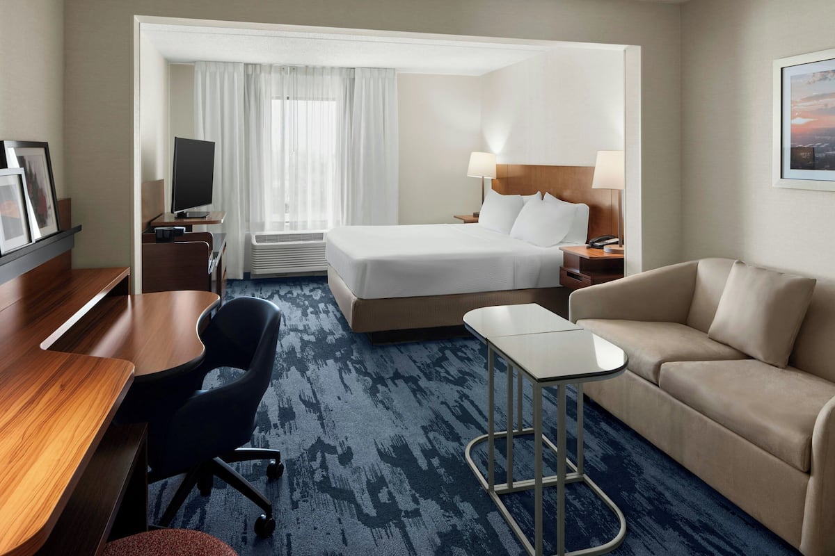 Une chambre d’hôtel équipée d’un lit, d’un bureau, d’une chaise, d’un canapé, d’une télévision et d’une fenêtre avec des rideaux.
